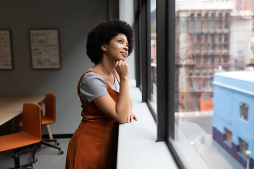 Mixed race businesswoman working in creative office. woman touching her chin and thinking. social distancing in workplace during covid 19 pandemic.