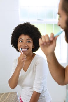 Diverse couple standing in bathroom brushing teeth. staying at home in isolation during quarantine lockdown.