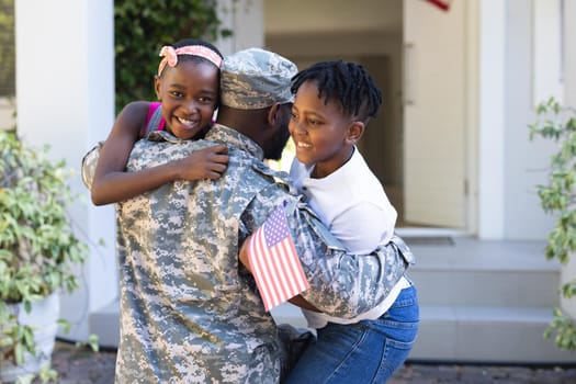 Rear view of african american soldier father hugging son and daughter in front of house. soldier returning home to family.