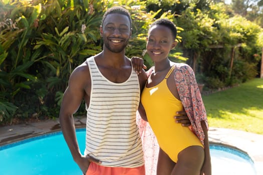 Portrait of african american couple smiling at the poolside on sunny garden terrace. staying at home in isolation during quarantine lockdown.