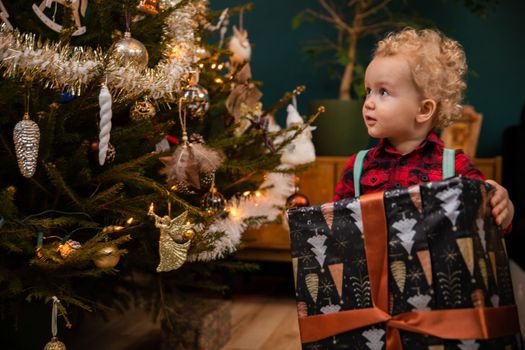 A happy little boy holds a big gift package in his hands. A happy childhood at Christmas too.