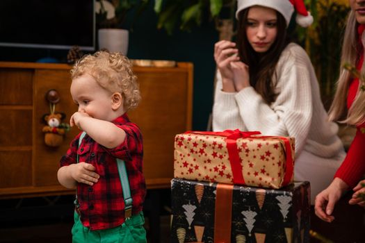 A two-year-old child looks at wrapped gift boxes standing next to a Christmas tree. Traditional Christmas in Poland.