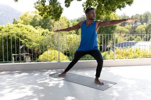 African american man exercising practicing yoga on sunny garden terrace. staying at home in isolation during quarantine lockdown.