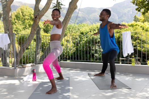 African american couple exercising practicing yoga on sunny garden terrace. staying at home in isolation during quarantine lockdown.
