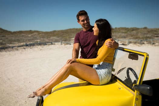 Happy caucasian couple by the sea smiling to each other, woman sitting on beach buggy. beach break on summer holiday road trip.