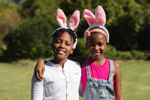 Portrait of happy african american brother and sister embracing wearing bunny ears outdoors. celebrating easter at home in isolation during quarantine lockdown.