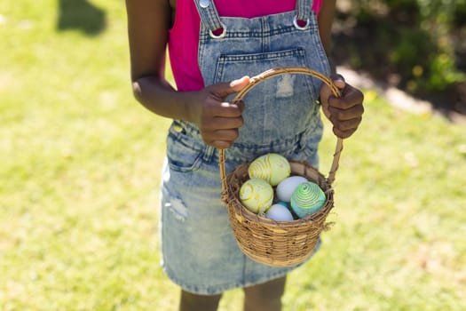 Midsection of african american girl holding basket while easter egg hunting. celebrating easter at home in isolation during quarantine lockdown.