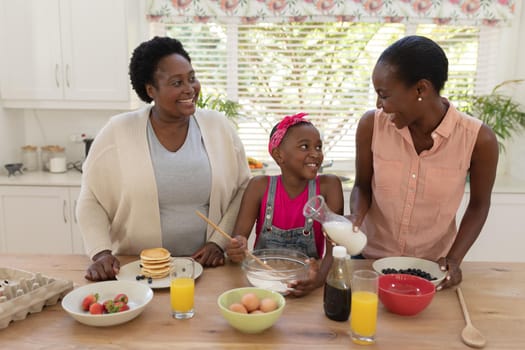 African american mother and grandmother teaching girl cooking in the kitchen. three generation family spending time together.