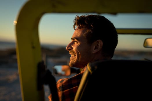 Happy caucasian man sitting in beach buggy by the sea during sunset smiling. beach break on summer holiday road trip