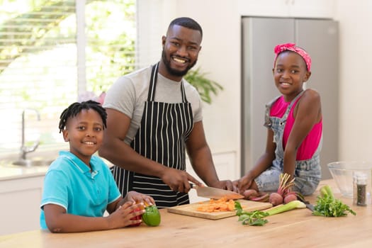 Happy african american father teaching daughter and son cooking in the kitchen. staying at home in isolation during quarantine lockdown.