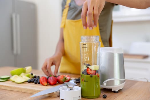Mixed race woman making a healthy drink and smiling in a kitchen. staying at home in isolation during quarantine lockdown.