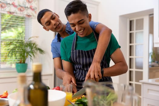 Diverse gay male couple spending time in kitchen cooking together and smiling. staying at home in isolation during quarantine lockdown.