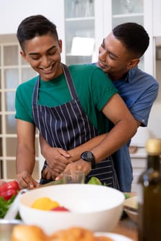 Diverse gay male couple spending time in kitchen embracing and smiling. staying at home in isolation during quarantine lockdown.