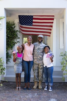 Smiling african american soldier father hugging wife and children in front of house. soldier returning home to family.