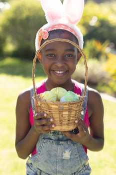 Portrait of african american girl holding basket while easter egg hunting. celebrating easter at home in isolation during quarantine lockdown.