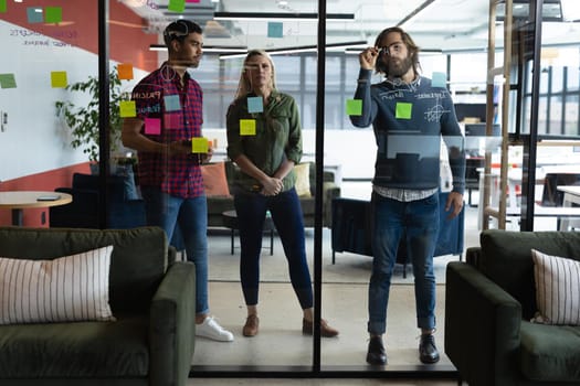 Diverse group of business people working in creative office. group of people brainstorming and taking notes on glass board. business people and work colleagues at a busy creative office.