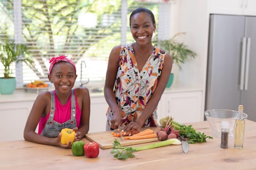 Portrait of happy african american mother teaching daughter cooking in the kitchen. staying at home in isolation during quarantine lockdown.