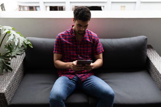 Mixed race businessman working in creative office. man sitting and using tablet. social distancing in workplace during covid 19 pandemic.