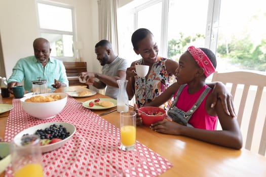 Happy african american parents, grandfather and granddaughter sitting at table and eating. three generation family spending quality time together.