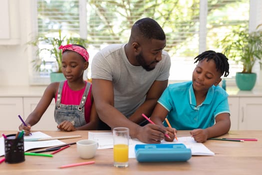 African american father sitting at table helping son and daughter with school work. staying at home in isolation during quarantine lockdown.