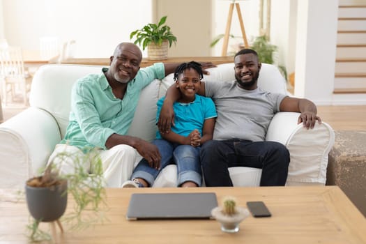Portrait of senior african american fon couch smiling with adult son and grandson embracing. happy three generation family spending time together at home.