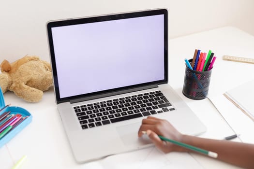 Hand of african american girl in bedroom using laptop with copy space for online school lesson. staying at home in isolation during quarantine lockdown.