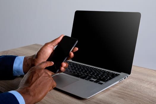 Close up of african american businessman using smartphone and laptop against grey background. business, professionalism and technology concept