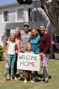 Happy caucasian soldier father, wife, children and parents outside home with welcome sign and flags. soldier returning home to family.