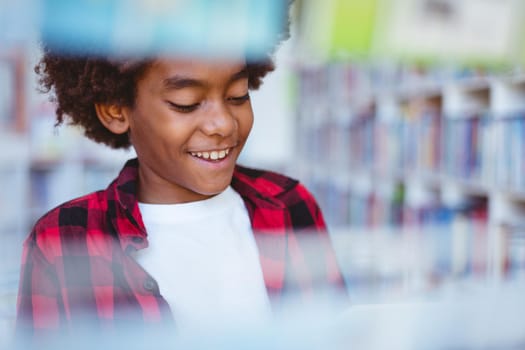 Laughing african american schoolboy reading book standing in school library. childhood and education at elementary school.