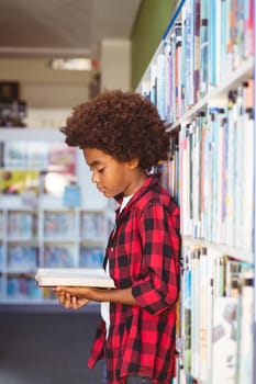 Happy african american schoolboy reading book standing in school library. childhood and education at elementary school.