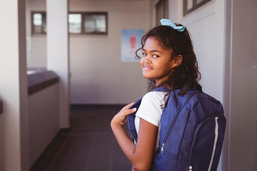 Portrait of smiling african american schoolgirl standing in school corridor wearing schoolbag. childhood and education at elementary school.