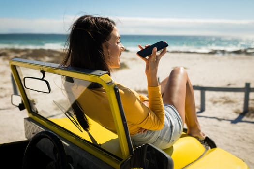 Caucasian woman lying on a beach buggy by the sea talking on smartphone. beach break on summer holiday road trip.