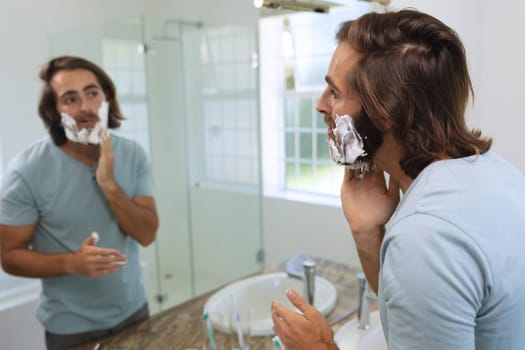 Caucasian man standing in bathroom applying shaving cream. staying at home in isolation during quarantine lockdown.