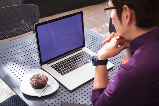 Asian businessman using laptop with blank screen sitting at table in cafe. digital nomad out and about in city concept.