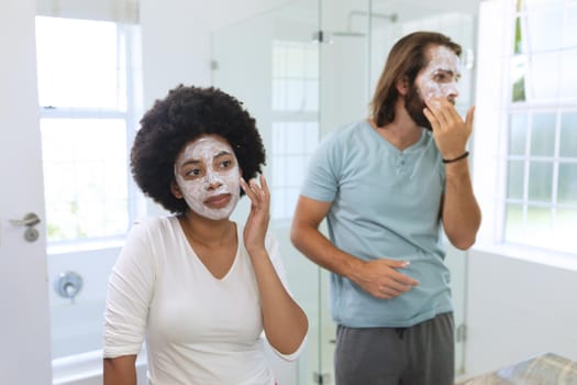 Diverse couple standing in bathroom wearing beauty masks. staying at home in isolation during quarantine lockdown.