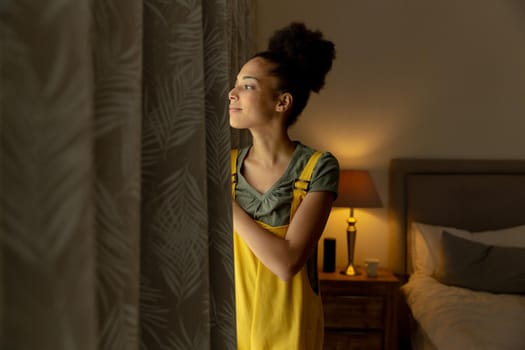 Mixed race woman standing by a window and smiling at home. staying at home in isolation during quarantine lockdown.