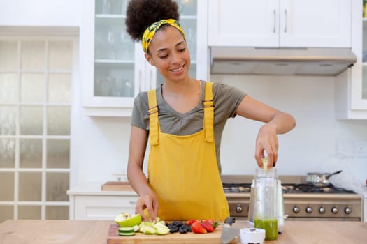 Mixed race woman making a healthy drink and smiling in a kitchen. staying at home in isolation during quarantine lockdown.