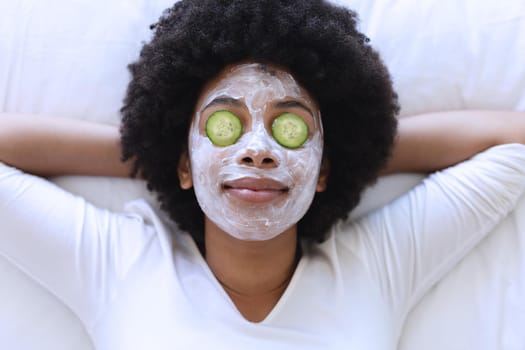 African american woman lying in bed wearing beauty mask. staying at home in isolation during quarantine lockdown.