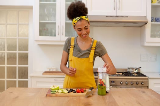 Mixed race woman making a healthy drink and smiling in a kitchen. staying at home in isolation during quarantine lockdown.