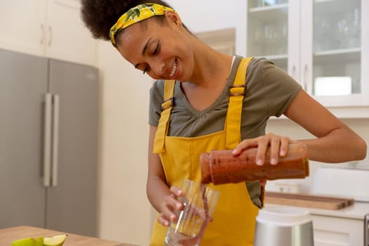 Mixed race woman pouring a healthy drink and smiling in a kitchen. staying at home in isolation during quarantine lockdown.