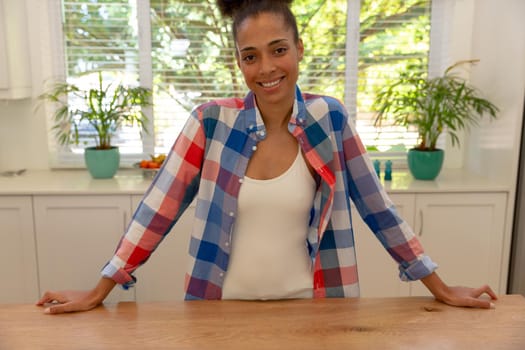 Mixed race woman looking at camera and smiling in a kitchen. staying at home in isolation during quarantine lockdown.
