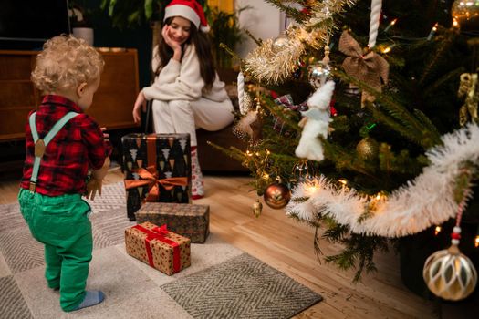 A child carries presents under the Christmas tree. Traditional Christmas in Poland. Little two year old boy with curly blonde hair.