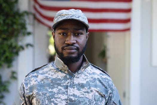 Portrait of african american male soldier standing in front of american flag outside home. soldier returning home to family.