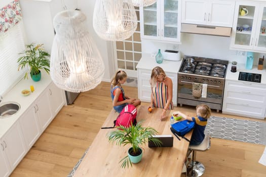 High angle view of caucasian mother with son and daughter preparing packed lunches in kitchen. happy family spending time together at home.