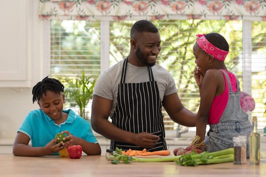 Happy african american father teaching daughter and son cooking in the kitchen. staying at home in isolation during quarantine lockdown.