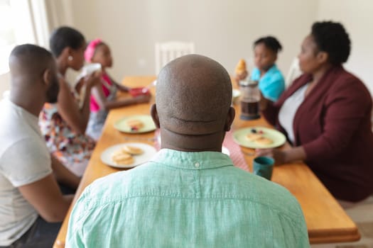 Happy african american parents, grandparents and grandchildren at table serving food and eating. three generation family spending quality time together.