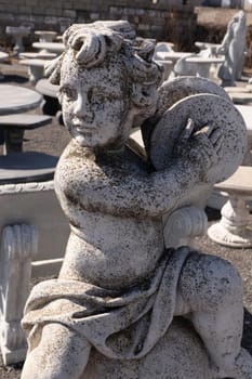 Ancient stone sculpture of naked cherub playing cymbals in reclamation yard. art and classical style romantic figurative stone sculpture.