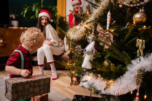 A two-year-old child looks at wrapped gift boxes standing next to a Christmas tree. Traditional Christmas in Poland.