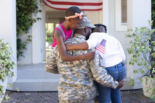 Rear view of african american soldier father hugging son and daughter in front of house. soldier returning home to family.