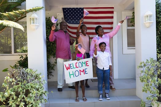 African american three generation family smiling outside home with american flags and welcome sign. soldier returning home to family.